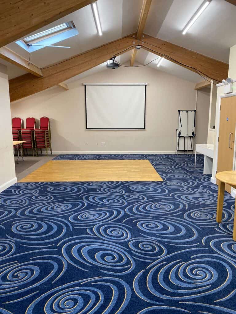 Modern community hall featuring a large projection screen, stacked chairs, and a vibrant blue patter.