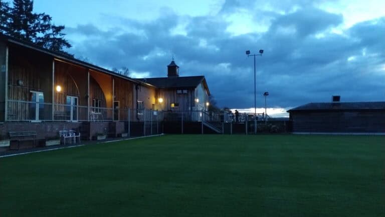 Outdoor sports field at dusk with illuminated hall in the background.