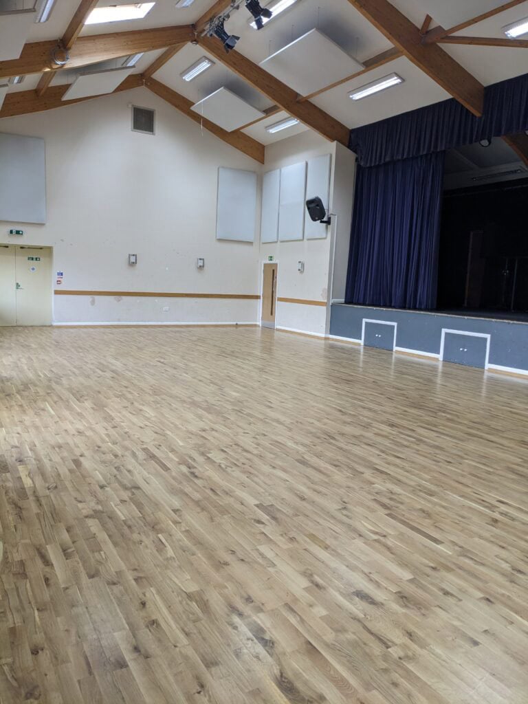 Bright main hall with polished wooden flooring and high ceilings, ideal for community events and gat.